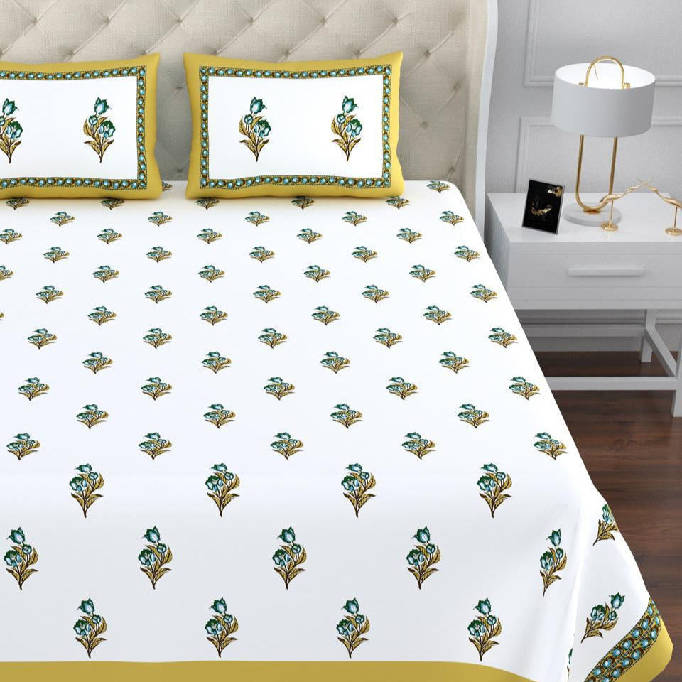 Bed with a white bedspread featuring green floral patterns and yellow borders, in a bedroom setting.