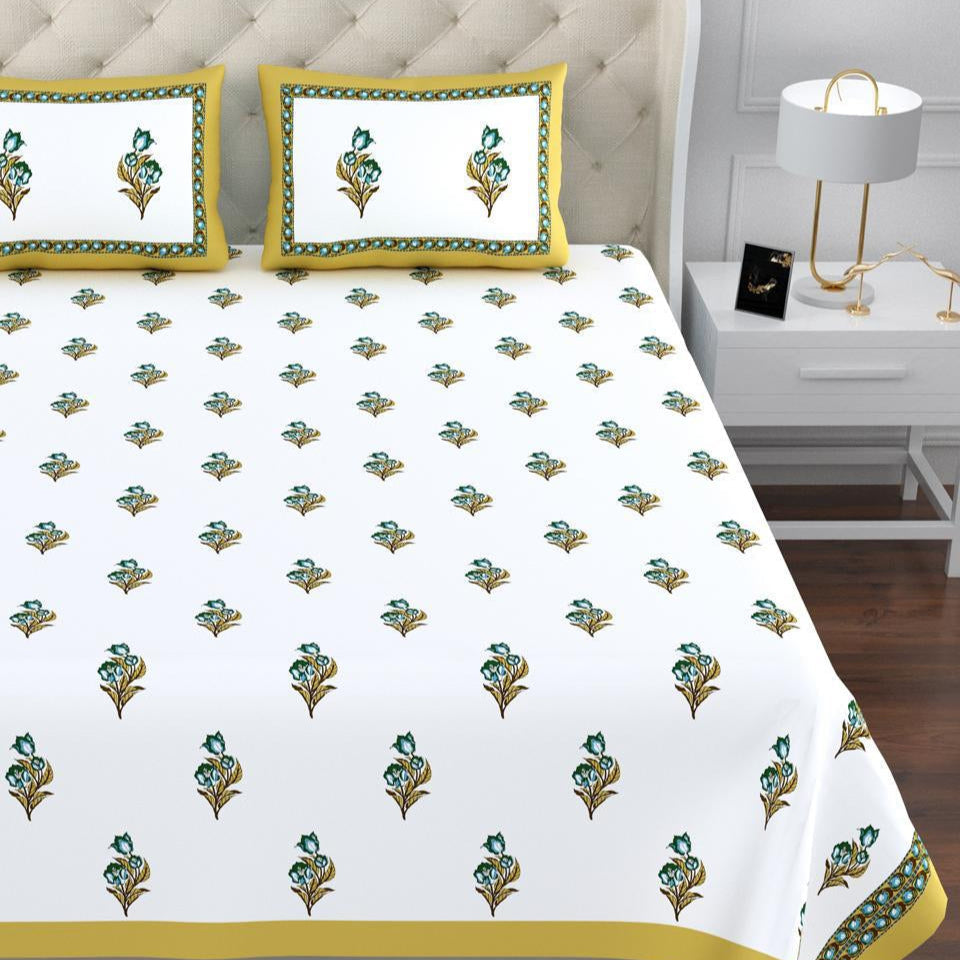 Bed with a white bedspread featuring green floral patterns and yellow borders, in a bedroom setting.