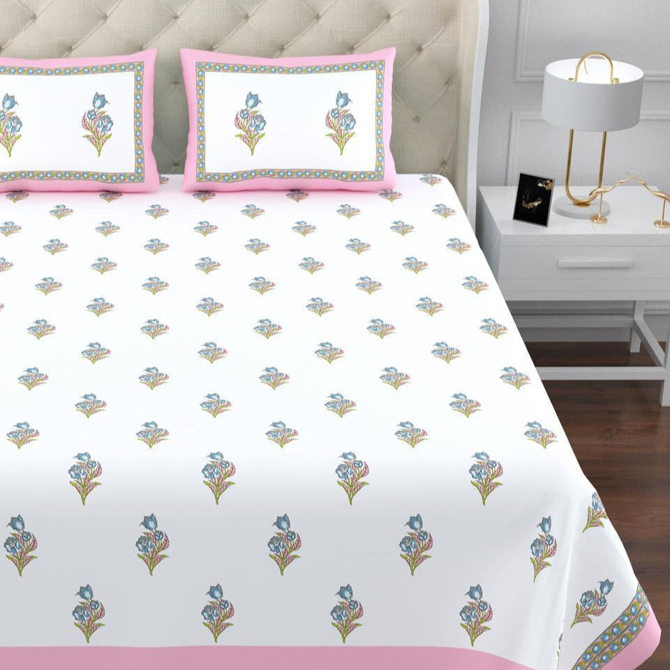 Floral patterned bedspread with pink border on a bed in a bedroom setting.