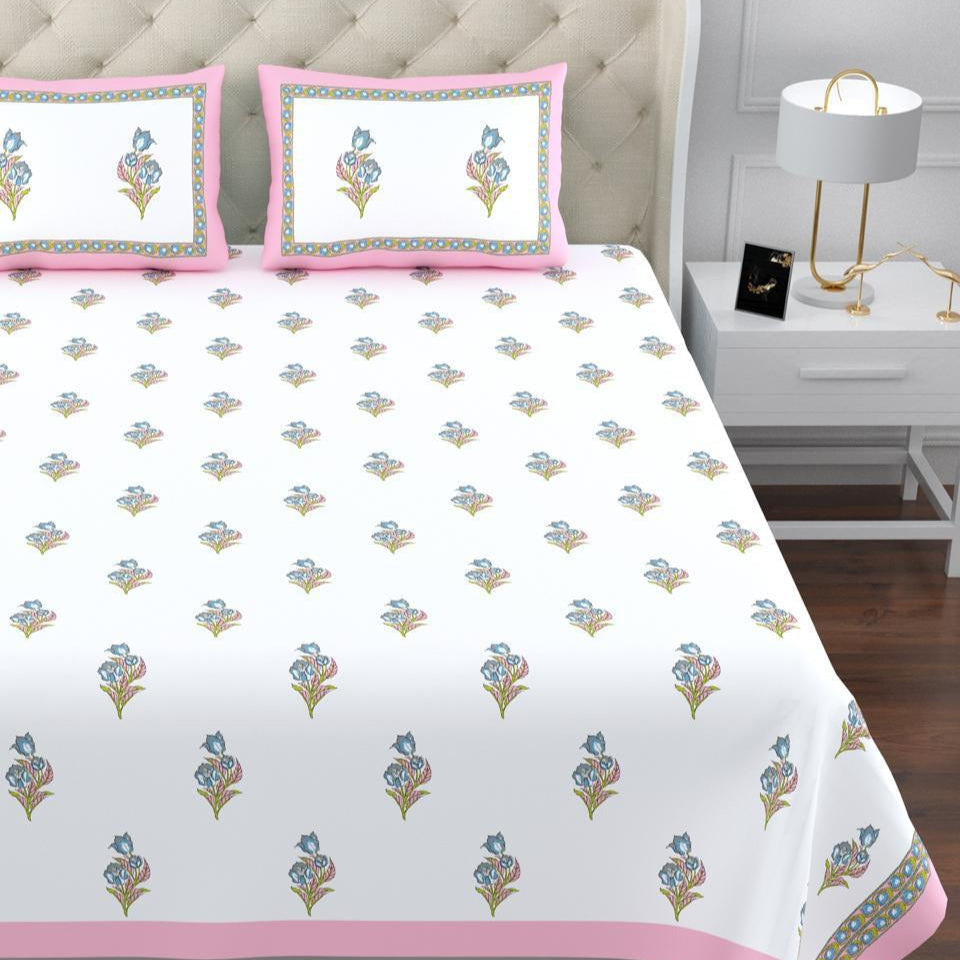 Floral patterned bedspread with pink border on a bed in a bedroom setting.