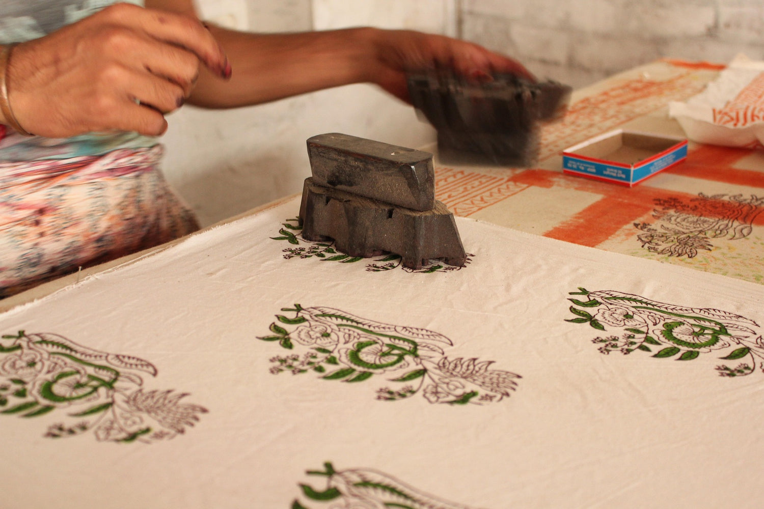 Person using a printing block on fabric with floral patterns